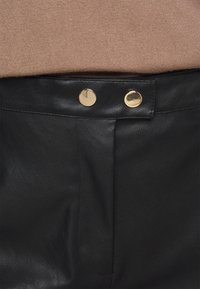 Svarta läderbyxor med en slät yta, två guldknappar i midjan och en välsydd frontveck.