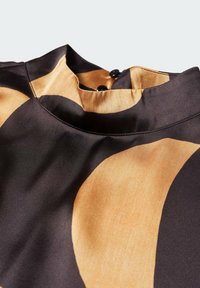 Blouse en satin avec un col montant, présentant des motifs abstraits noirs et brun doré. Fermeture par boutons dans le dos.