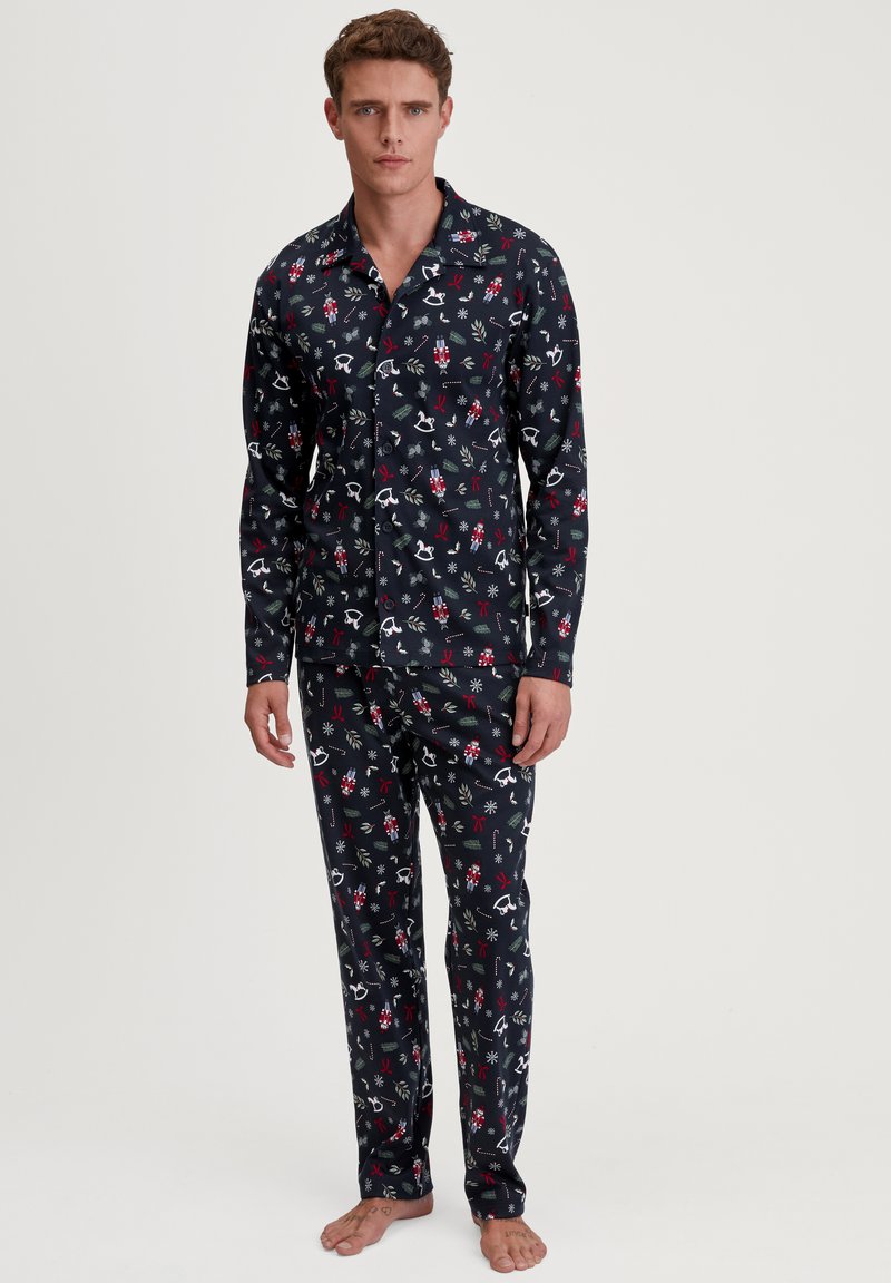 Navyblaues Pyjama-Set mit einem Knopfverschluss-Hemd und einer Hose, verziert mit einem festlichen Muster aus winterlichen Illustrationen in Rot und Weiß.