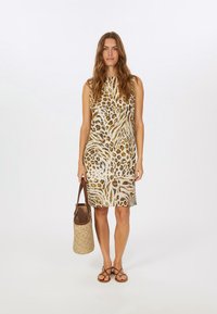Ärmelloses Kleid mit Leopardenmuster in Erdtönen auf einem hellen Hintergrund, ergänzt durch eine geflochtene Tasche und flache Sandalen.