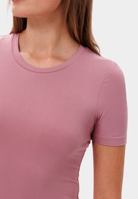 Růžové, přiléhavé tričko s krátkým rukávem a kulatým výstřihem se hladkým povrchem. Lehce žebrovaná tkanina s jemným leskem.
