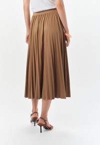 Brąskowa plisowana spódnica midi z marszczoną talią. Materiał jest gładki, a spódnica ma rozkloszowany krój, uzupełniony o sandały na obcasie.