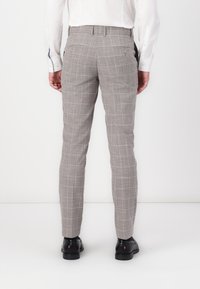 Graue Karohosen im Slim-Fit-Schnitt, aus einem strukturierten Stoff gefertigt, mit zwei hinteren Taschen mit Knöpfen und schwarzen Schuhen.