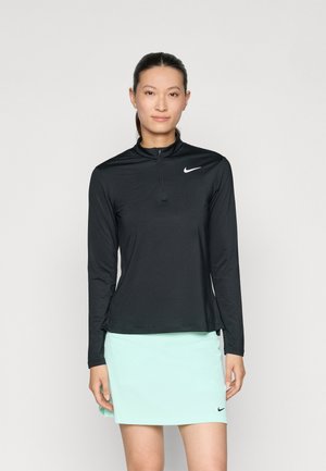 Chemise zippée noire à manches longues avec une finition texturée, associée à une jupe vert menthe clair ; présente un petit logo Nike blanc sur la chemise.