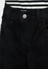 Μαύρο τζιν παντελόνι με εφαρμοστή σχεδίαση, με κλείσιμο με ασημένιο κουμπί, διακριτή υφή και πλαϊνές τσέπες. Φοράει ριγέ πουκάμισο εμφανές στην κορυφή.