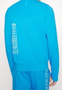 Bright blue sweatshirt, crew neck, long sleeves. Features white text logo along the right sleeve and side. Soft, smooth fabric texture.