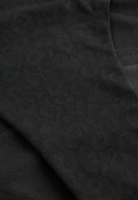 Tissu noir avec un motif léopard subtil, présentant une surface texturée et des sections de matériau lisse.