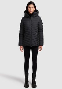 Black puffer jacket with a hood, featuring horizontal quilted sections, two side zip pockets, and a front zipper. Worn with black leggings and boots.