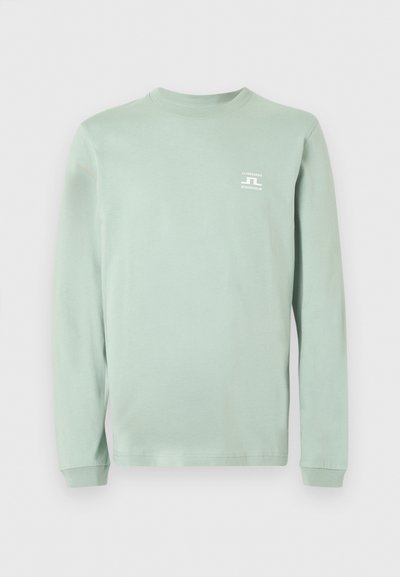 Φωτεινό πράσινο μακρυμάνικο μπλουζάκι με στρογγυλή λαιμόκοψη και μικρό λευκό λογότυπο "J.LINDEBERG STOCKHOLM" στο πάνω αριστερό μέρος του στήθους.