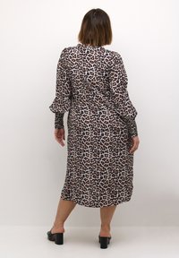 Robe midi à imprimé léopard en tissu léger, avec des manches longues à poignets froncés et une silhouette décontractée. Sandales à talons blocs noires.