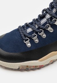 Marinblå mocka och svart läder sneakers med silver ögla, mönstrade snören och en strukturerad flerfärgad sula. Taperad design, förstärkt tåområde.