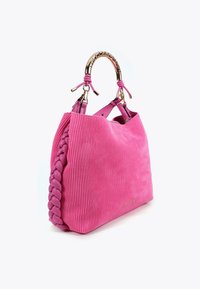 Borsa texture rosa con manico intrecciato e dettagli in oro, posizionata in un angolo su uno sfondo bianco.