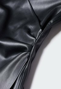 Tissu en cuir noir lisse avec coutures visibles et plis naturels sur un fond clair, mettant en valeur la texture et la qualité du matériau.