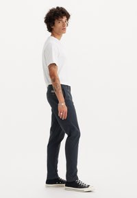 Hvid kortærmet T-shirt parret med mørkeblå bukser. Bukserne er lige snit med en subtil tekstur. Sorte sneakers fuldender outfittet.