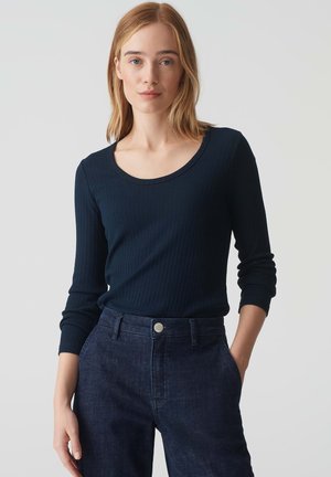 Marineblauw geribbeld langemouwen shirt met een ronde hals, gecombineerd met donkerblauwe broek. De stof is gestructureerd, met een aansluitende pasvorm en subtiele glans.
