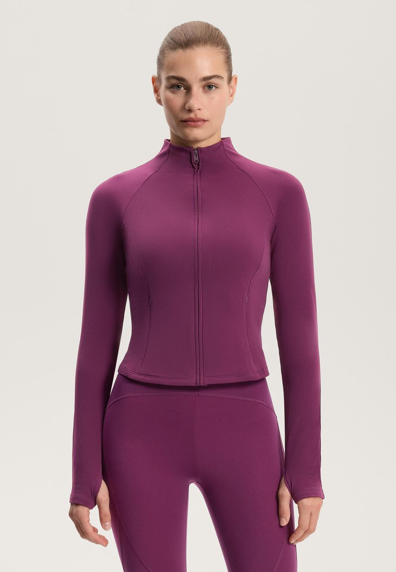 Přiléhavá fialová sportovní bunda s vysokým límcem a plným zipem, dlouhými rukávy a otvory na palce; vyrobená z pružné, hladké tkaniny.