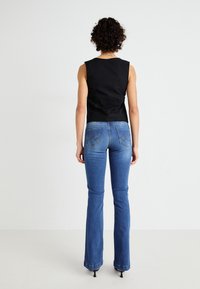 Haut noir sans manches associé à un jean évasé bleu. Le jean présente un design subtil sur la poche arrière et une finition légèrement délavée.