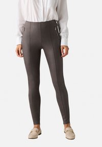 Leggings gris de cintura alta con bolsillos laterales con cremallera, textura suave y un diseño ajustado, combinados con una camisa blanca de botones y zapatos tipo slip-on.