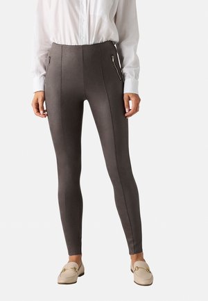 Leggings gris de cintura alta con bolsillos laterales con cremallera, textura suave y un diseño ajustado, combinados con una camisa blanca de botones y zapatos tipo slip-on.