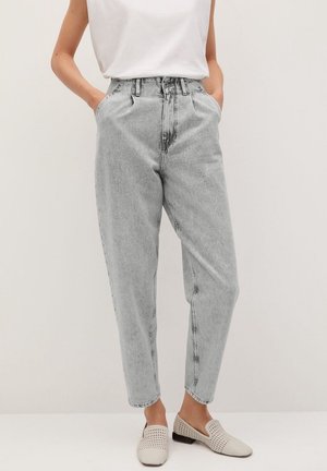 Personne portant un jean en denim gris clair taille haute avec jambes fuselées, un haut blanc sans manches et des chaussures beige tissées sans lacets. Mains dans les poches.
