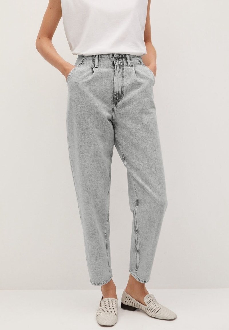 Personne portant un jean en denim gris clair taille haute avec jambes fuselées, un haut blanc sans manches et des chaussures beige tissées sans lacets. Mains dans les poches.