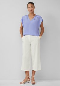 Lichtpaarse bloes met korte mouwen en v-hals; gecombineerd met witte wijde broek en sandalen met een lage hak.