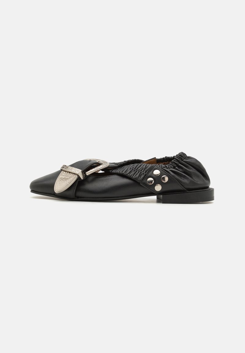 Zapato plano de cuero negro con punta afilada, diseño fruncido en el talón, detalle de hebilla plateada y tachuelas decorativas plateadas en el lateral.