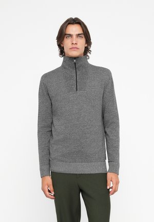Grauer Reißverschluss-Pullover mit strukturiertem Strickmuster, hohem Kragen und geripptem Saum. Getragen mit dunkelgrünen Hosen.