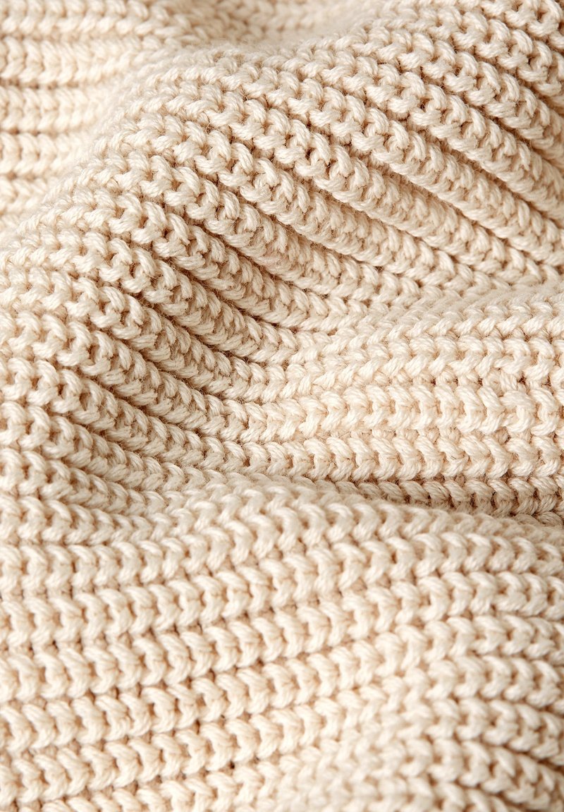 Tela beige tejida con puntadas texturizadas y elevadas dispuestas en un patrón de ondas, que muestra una apariencia suave y acogedora.