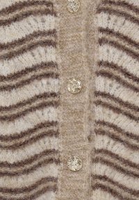 Gros plan d’un tissu tricoté rayé beige et marron avec une rangée verticale de boutons dorés texturés.