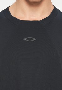 Σκούρο ναυτικό μπλουζάκι κοντού μανικιού με στρογγυλή λαιμόκοψη. Έχει ένα μικρό τονικό λογότυπο στο κέντρο του στήθους. Λείο, μαλακό υλικό.