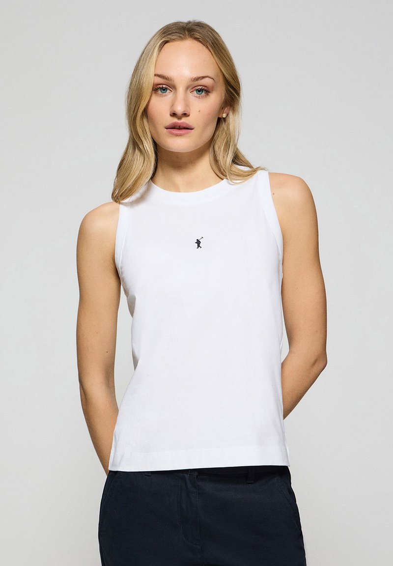 Vit ärmlös topp med rund hals och en liten mörk logotyp på bröstet. Tillverkad av en mjuk bomullsblandning med en avslappnad passform.