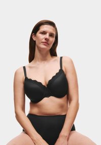 Sujetador negro acolchado con borde de encaje, con tirantes ajustables y diseño sin costuras. Combinado con una braguita negra de talle alto.