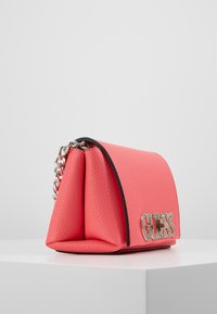 Borsa a mano in pelle sintetica corallo con design strutturato, accentuata da una catena argentata e logo "GUESS" in rilievo sulla parte anteriore, caratterizzata da una texture liscia.