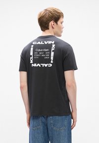 Μαύρη βαμβακερή μπλούζα T-shirt με έντονο λευκό κείμενο "Calvin Klein" και διεύθυνση τυπωμένη στην πλάτη, με άνετη εφαρμογή και κοντά μανίκια.