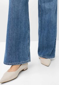 Light blue wide-leg jeans made from denim, with a frayed hem, paired with cream-colored flat shoes featuring a pointed toe design.