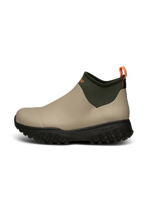 Beige vedenpitävät nilkkakengät, joissa on tummanvihreä kaulus, teksturoitu kumipohja ja oranssi vetotappi takana.