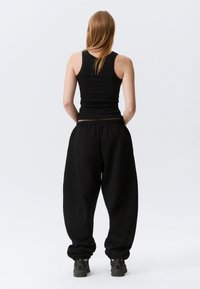 Débardeur noir sans manches et pantalon de survêtement noir ample avec une taille élastique, présentant une coupe décontractée et des poignets resserrés.