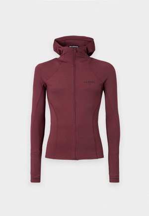 Veste zippée bordeaux avec capuche, design ajusté, manches longues et logo noir minimaliste brodé sur la poitrine. Texture de tissu douce.