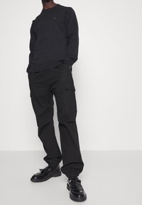 Czarna bawełniana koszulka z długim rękawem z małym logo, zestawiona z luźnymi czarnymi spodniami cargo z bocznymi kieszeniami i teksturowanym wykończeniem. Czarne buty.