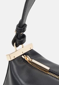 Schwarze Lederhandtasche mit einem goldfarbenen Hardware-Verschluss und Reißverschluss. Sie verfügt über einen geknoteten Tragegurt und eine glatte Textur.