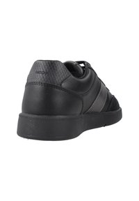 Zapatilla negra de cuero con acentos texturizados, que presenta un acabado suave, una franja gris en contraste y una suela de goma. Marca Geox visible.