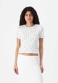 Vit kortärmad t-shirt med ribbad textur, med ett blått blommönster, kort design och rund halsringning.
