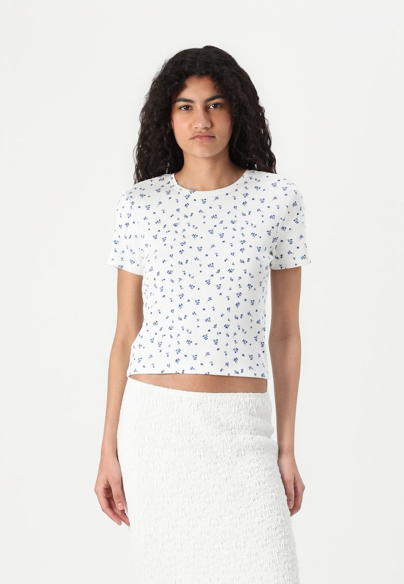Vit kortärmad t-shirt med ribbad textur, med ett blått blommönster, kort design och rund halsringning.