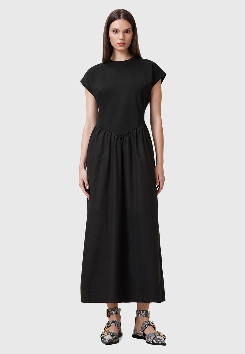 Vestido negro de algodón con mangas cortas, cuerpo ajustado y cintura fruncida. Textura suave, hasta el tobillo, combinado con sandalias estampadas.
