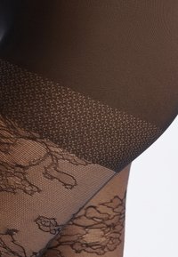 Zwarte sheer panty met een gestructureerde, gedessineerde bovenband en een ingewikkeld bloemmotief langs het been, wat zorgt voor een delicate en elegante uitstraling.