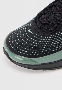 Shoe atlético preto com parte superior em rede texturizada, destaques em verde menta e uma entressola brilhante. Possui perfurações circulares para ventilação.