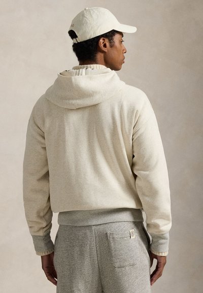 Μπεζ φούτερ με διπλωμένη κουκούλα και ριμπ λεπτομέρειες, συνδυασμένο με γκρίζα φόρμα που διαθέτει πίσω τσέπη και ταμπέλα λογότυπου.