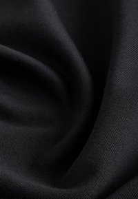 Primer plano de tela negra con textura de punto fino, suavemente doblada para mostrar la profundidad y el detalle de la superficie del material.