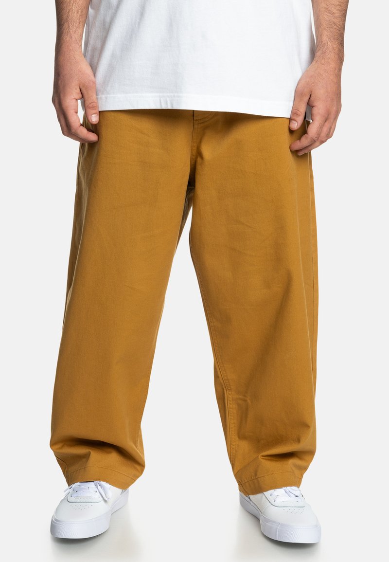 Gule bomuldsbukser med bredde ben, der har en glat tekstur og en afslappet pasform, parret med hvide sneakers. Enkel design uden synlige mønstre.